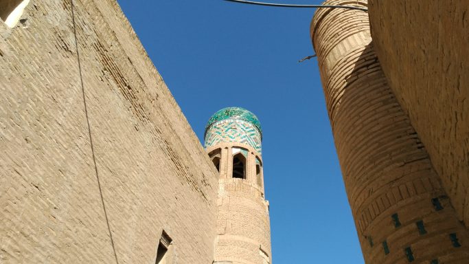 Vista de una torre con cúpula verde entre muros de adobe bajo un cielo azul.