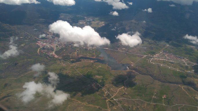 Paisaje aéreo de campos, ríos y nubes, con una zona urbana al fondo.